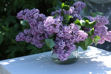 Photo of Beautiful lilac flowers in vase on table in garden