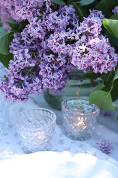 Photo of Beautiful lilac flowers, plates and burning candles on table in garden, closeup