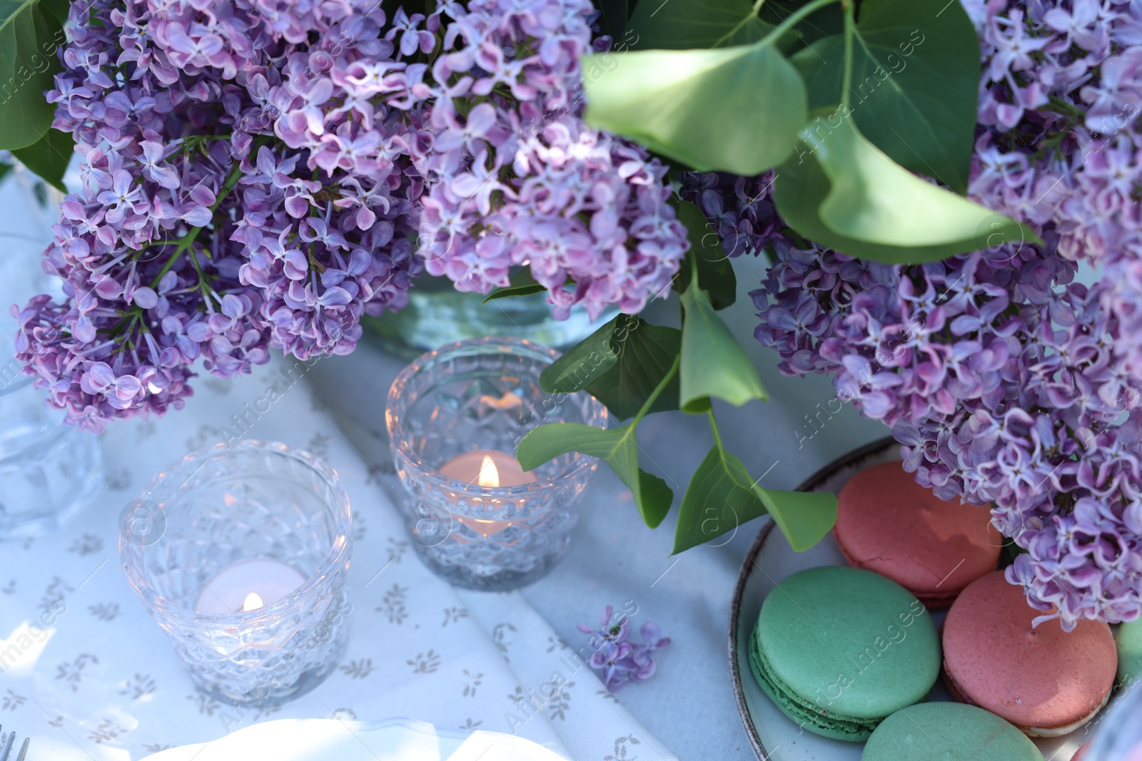 Beautiful lilac flowers, sweets and burning candles on table in garden, above view Photo of Beautiful lilac flowers, sweets and burning candles on table in garden, above view