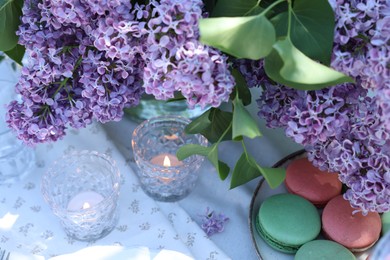 Photo of Beautiful lilac flowers, sweets and burning candles on table in garden, above view