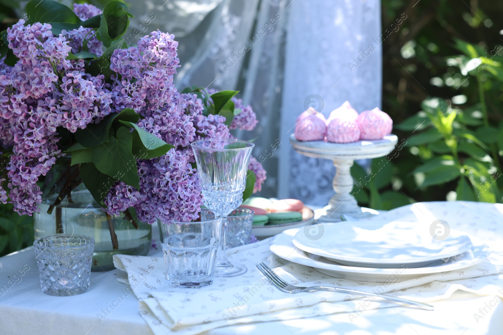 Beautiful lilac flowers, sweets, plates, cutlery and glasses on table in garden Photo of Beautiful lilac flowers, sweets, plates, cutlery and glasses on table in garden