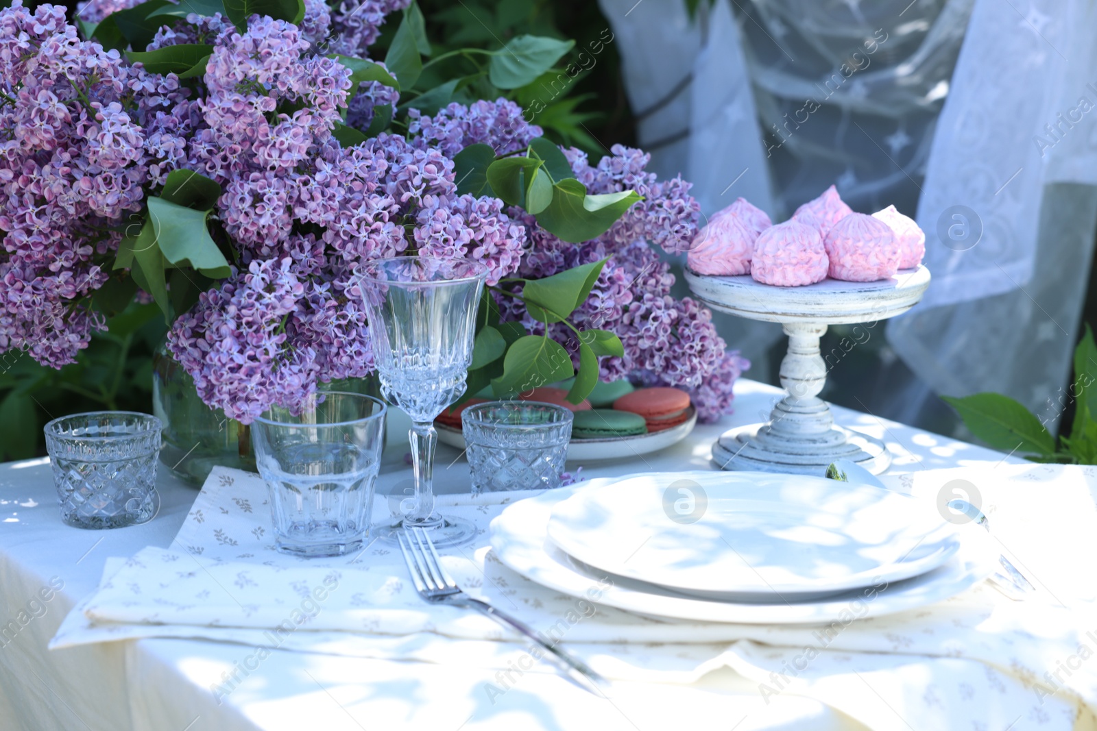 Beautiful lilac flowers, sweets, plates, cutlery and glasses on table in garden Photo of Beautiful lilac flowers, sweets, plates, cutlery and glasses on table in garden