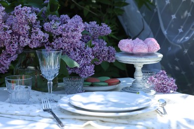 Photo of Beautiful lilac flowers, sweets, plates, glasses and cutlery on table in garden