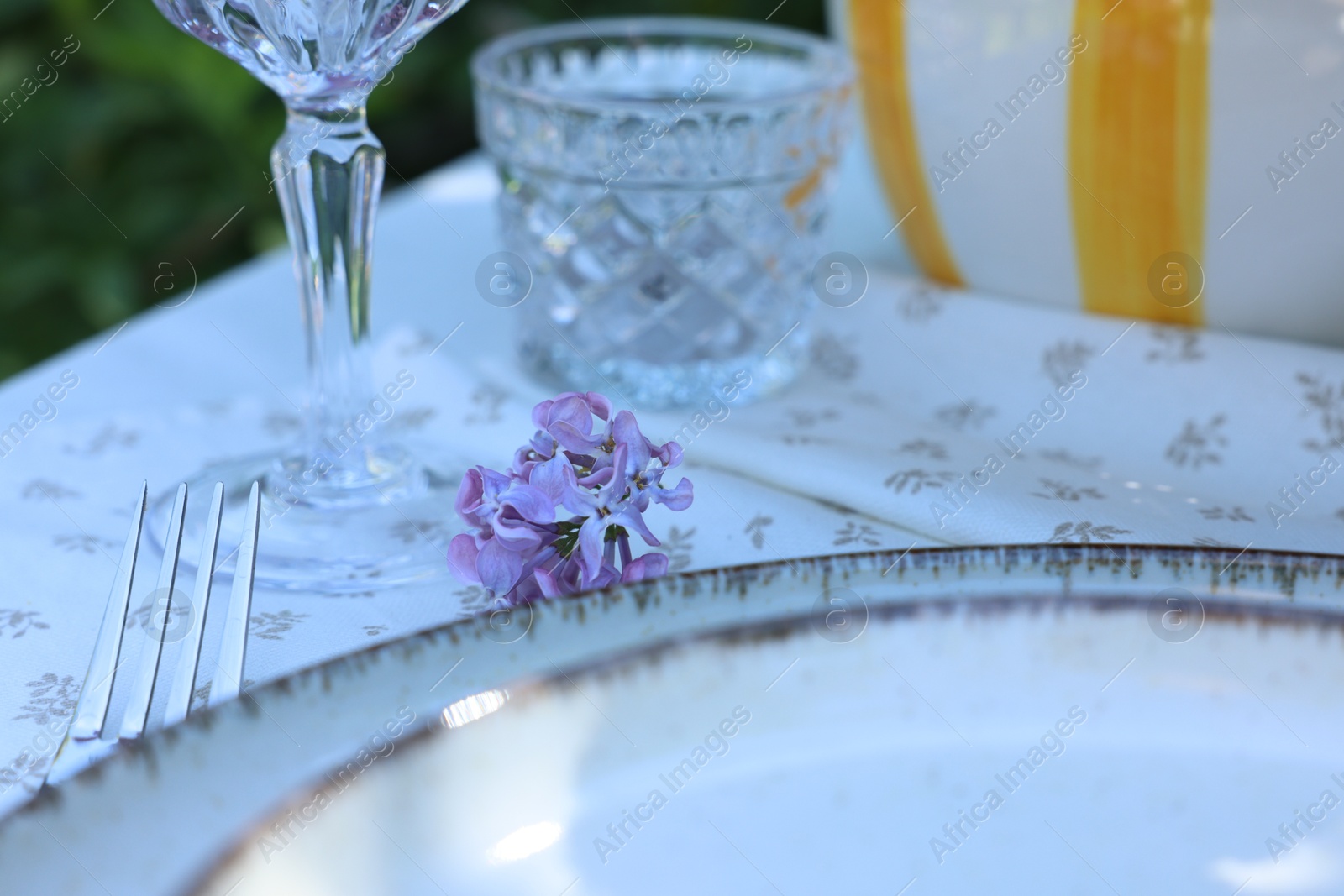 Beautiful lilac flowers, plates, glasses and fork on table, closeup Photo of Beautiful lilac flowers, plates, glasses and fork on table, closeup