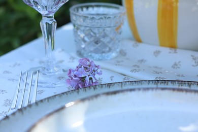Photo of Beautiful lilac flowers, plates, glasses and fork on table, closeup