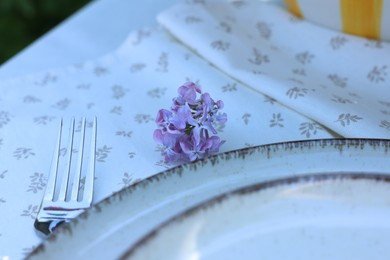 Photo of Beautiful lilac flowers, plates and fork on table, closeup