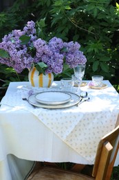 Photo of Beautiful lilac flowers, plates, cutlery, glasses and candles on table in garden
