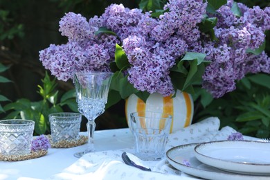 Photo of Beautiful lilac flowers, plates, glasses, spoon and candles on table in garden