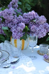 Photo of Beautiful lilac flowers, glasses, cutlery and candle on table in garden