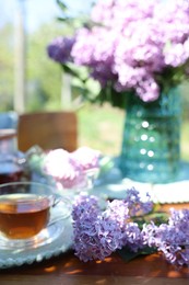 Photo of Beautiful lilac flowers and tea on table in garden, closeup