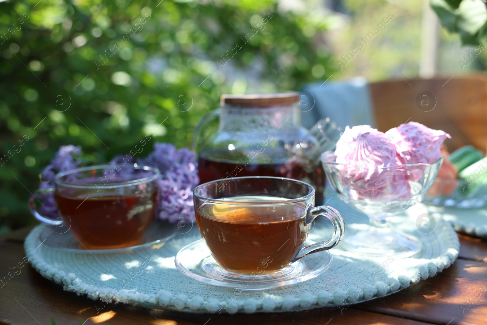 Aromatic tea in cups, teapot, zephyrs and lilac flowers on wooden table in garden, closeup Photo of Aromatic tea in cups, teapot, zephyrs and lilac flowers on wooden table in garden, closeup