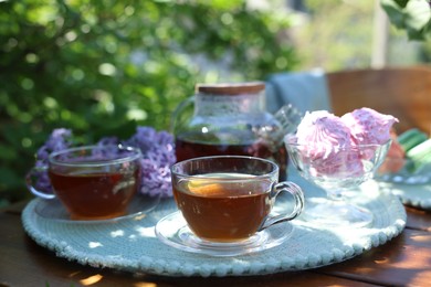 Photo of Aromatic tea in cups, teapot, zephyrs and lilac flowers on wooden table in garden, closeup