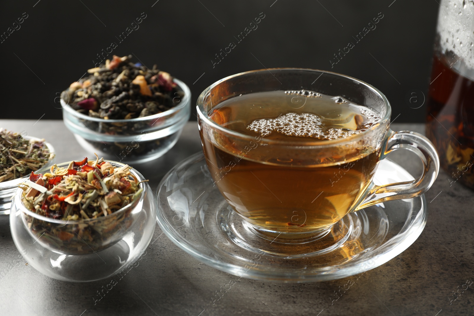 Refreshing herbal tea and dry leaves on grey table, closeup Photo of Refreshing herbal tea and dry leaves on grey table, closeup