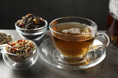 Photo of Refreshing herbal tea and dry leaves on grey table, closeup