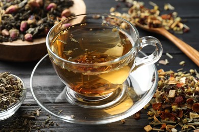 Photo of Refreshing herbal tea and dry leaves on black wooden table, closeup