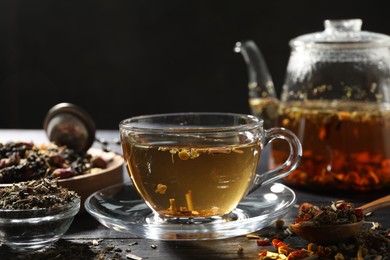 Photo of Refreshing herbal tea and dry leaves on black wooden table, closeup. Space for text