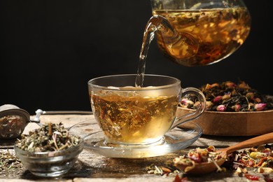 Photo of Pouring herbal tea from teapot into cup at wooden table, closeup. Space for text