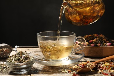 Photo of Pouring herbal tea from teapot into cup at wooden table, closeup. Space for text