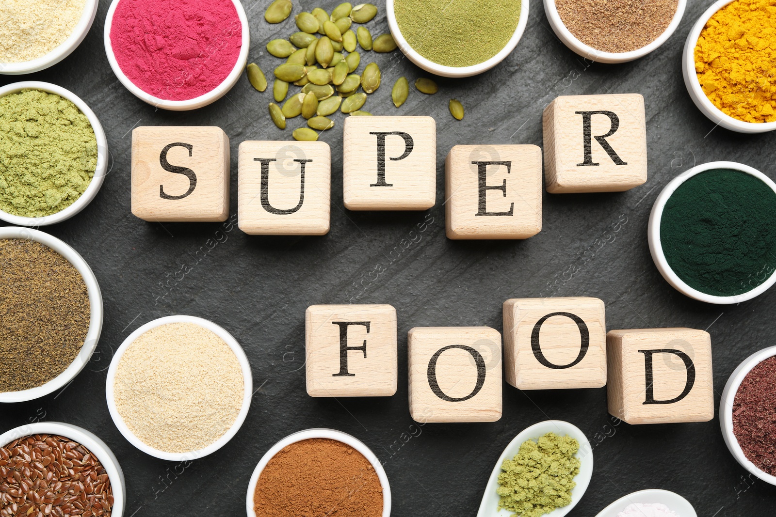 Photo of Different superfood powders and words made of cubes on black table, flat lay