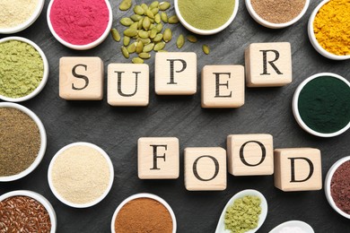 Photo of Different superfood powders and words made of cubes on black table, flat lay