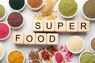 Photo of Different superfood powders and words made of cubes on light grey table, flat lay