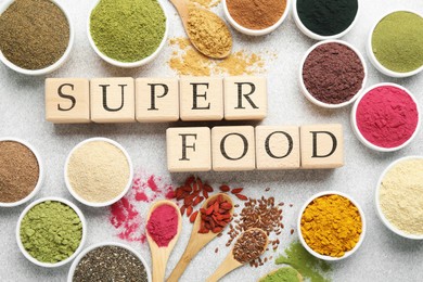 Photo of Different superfood powders and words made of cubes on light grey table, flat lay