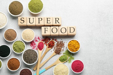 Photo of Different superfood powders and words made of cubes on light grey table, flat lay. Space for text