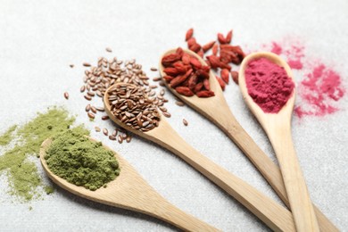 Photo of Different superfood powders in spoons on light grey table, closeup