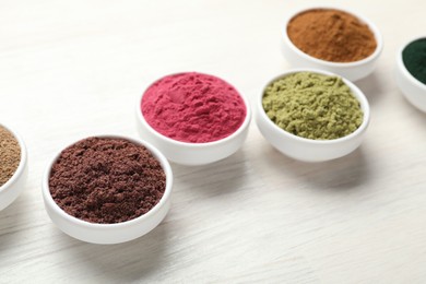 Photo of Different superfood powders on white wooden table, closeup