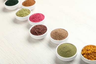 Photo of Different superfood powders on white wooden table, closeup