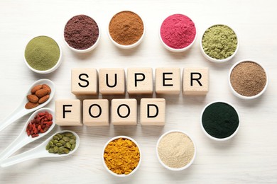 Photo of Different superfood powders and words made of cubes on white table, flat lay