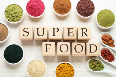 Photo of Different superfood powders and words made of cubes on white table, flat lay