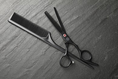 Photo of Comb and scissors on black table, flat lay. Hairdresser's tools