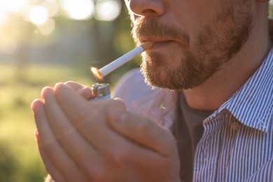 Photo of Man lighting cigarette with lighter outdoors, closeup