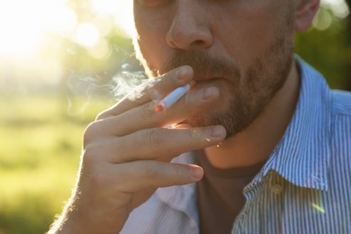 Photo of Man smoking cigarette outdoors on sunny day, closeup