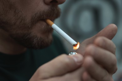 Photo of Man lighting cigarette on blurred background, closeup