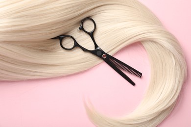 Photo of Hair strand and scissors on light pink background, top view