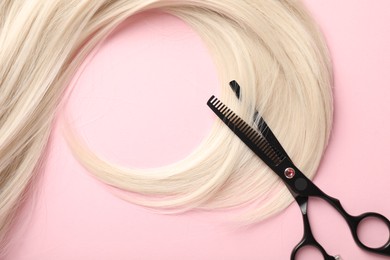 Photo of Hair strand and scissors on light pink background, top view