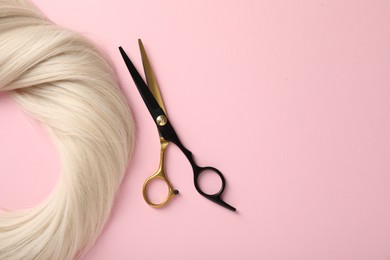 Photo of Hair strand and scissors on light pink background, top view. Space for text
