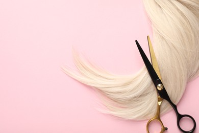 Photo of Hair strand and scissors on light pink background, top view. Space for text