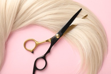 Photo of Hair strand and scissors on light pink background, top view