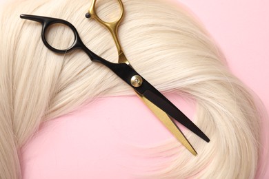 Photo of Hair strand and scissors on light pink background, top view