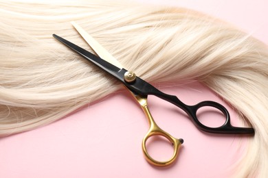 Photo of Hair strand and scissors on light pink background, closeup