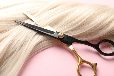 Photo of Hair strand and scissors on light pink background, closeup