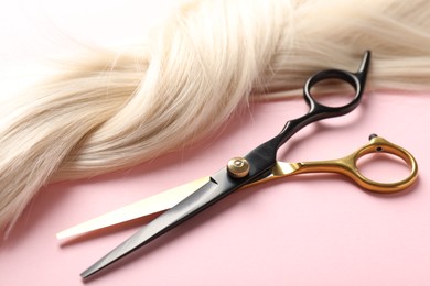 Photo of Hair strand and scissors on light pink background, closeup