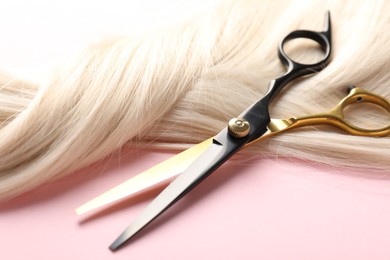 Photo of Hair strand and scissors on light pink background, closeup