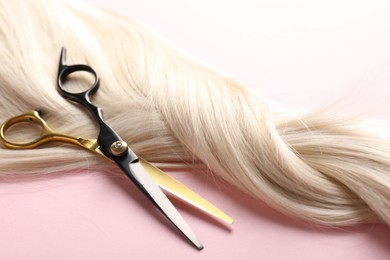 Photo of Hair strand and scissors on light pink background, closeup