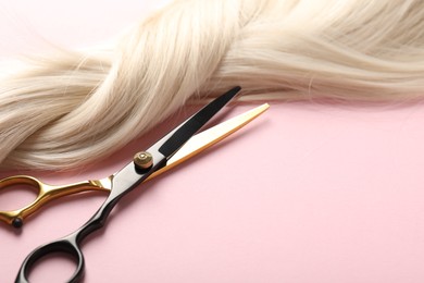 Photo of Hair strand and scissors on light pink background, closeup. Space for text