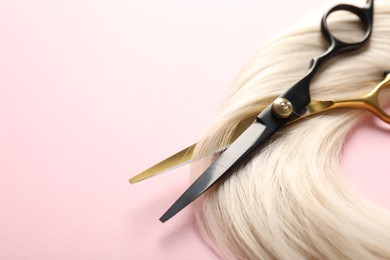 Photo of Hair strand and scissors on light pink background, closeup. Space for text