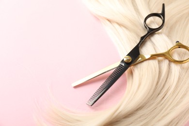 Photo of Hair strand and scissors on light pink background, closeup. Space for text